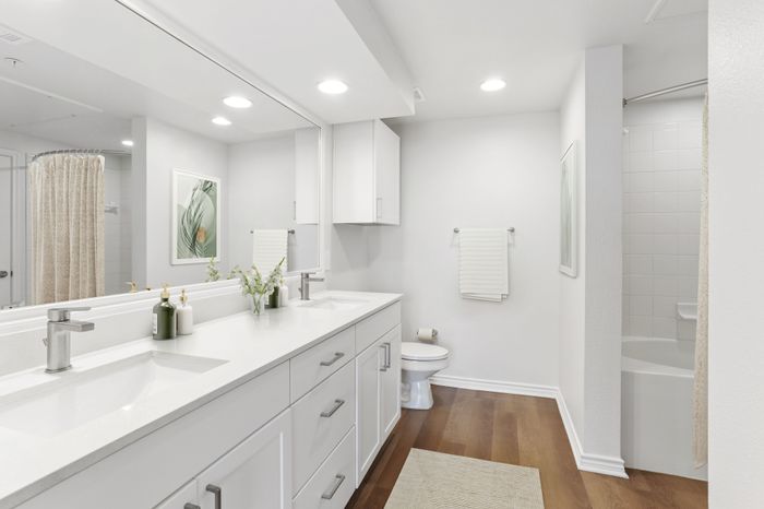 Large bathroom with a large, well lit mirror, two sink basins, white countertops, tiled shower and bathtub, and wood-style plank flooring at Lantower Residences at the Collection