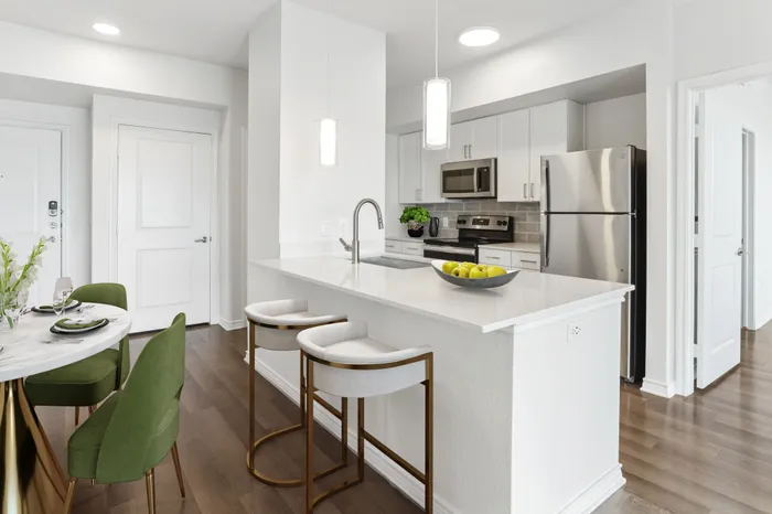 Spacious living and dining room with room for plenty of furniture, connected to Modern kitchen fit with white countertops and stainless steel sink basin, stainless steel appliances, and a counter with overhead lighting at Lantower Residences at the Collection
