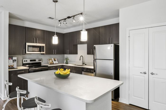 Chef-inspired kitchen with brushed nickel fixtures, 9-foot ceilings, Arctic Ice Quartz countertops and a kitchen island at Lantower Brandon Crossroads decorated with modern barstools and a bowl of fruit.