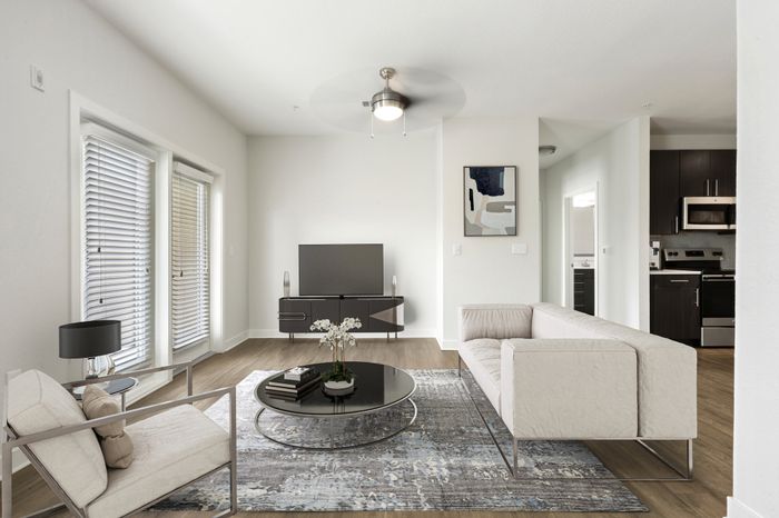 Living room with hardwood style-flooring, two large windows with natural sunlight, access to a private balcony and modern cream-colored furniture at Lantower Brandon Crossroads.