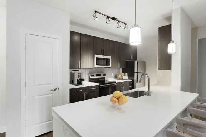 Chef-inspired kitchen with brushed nickel fixtures, 9-foot ceilings, Arctic Ice Quartz countertops and a kitchen island at Lantower Brandon Crossroads decorated with modern barstools and a bowl of fruit.