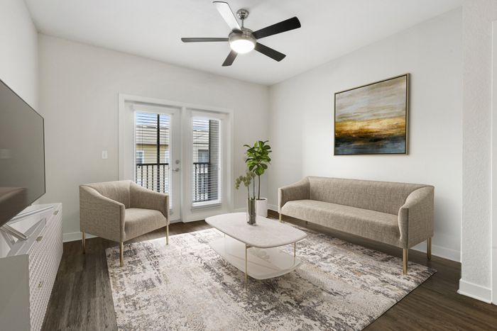 Living room with hardwood style-flooring, two large windows with natural sunlight, access to a private balcony and modern cream-colored furniture at Lantower Brandon Crossroads.