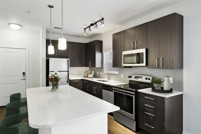 Chef-inspired kitchen with brushed nickel fixtures, 9-foot ceilings, Arctic Ice Quartz countertops and a kitchen island at Lantower Brandon Crossroads decorated with modern barstools and a bowl of fruit.