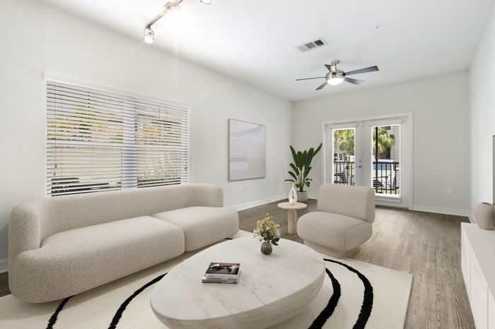 Spacious, naturally lit living room with hardwood-style floors, two large windows, glass doors leading to a private balcony and unique, modern furniture at Lantower Brandon Crossroads.