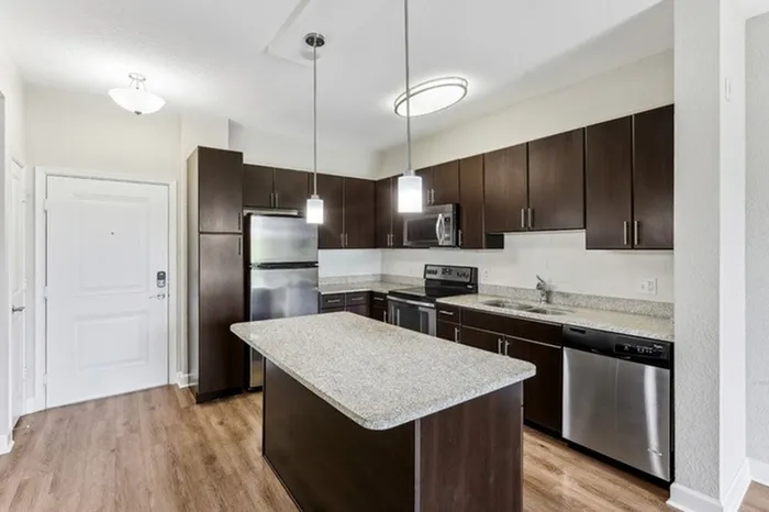 Kitchen with granite countertops, espresso-colored cabinetry, stainless steel appliances with glass cooktop, white tile backsplash, pendant lighting, and large island at Lantower Westshore.