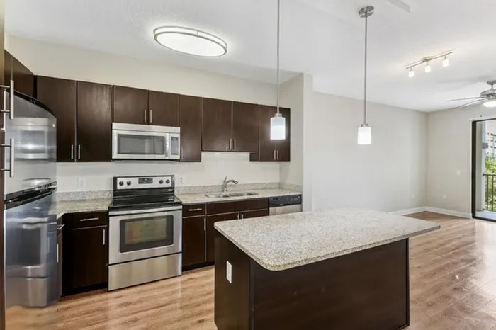 Open-concept kitchen with granite countertops, espresso-colored cabinets, stainless steel appliances, white tile backsplash, pendant lighting, and large island at Lantower Westshore.