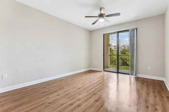 Spacious open-concept living area with view of kitchen, wood-style flooring, ceiling fan, and ample natural light from sliding door leading to private patio at Lantower Westshore.