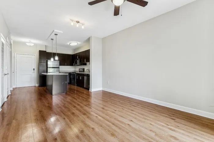 Spacious open-concept living area with view of kitchen, wood-style flooring, ceiling fan, and ample natural light from sliding door leading to private patio at Lantower Westshore.