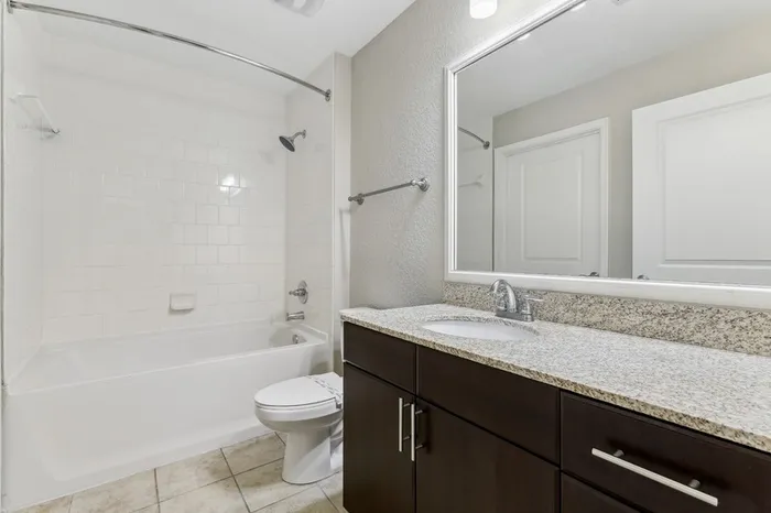 Large and bright bathroom with granite countertop, espresso-colored cabinetry, large mirror, tile flooring, and tiled shower tub combo at Lantower Westshore.