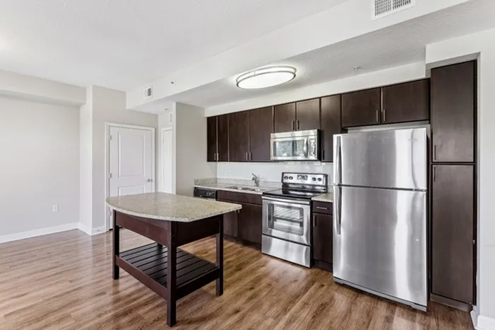 Spacious open-concept kitchen with granite countertops, espresso-colored cabinets, stainless steel appliances, white tile backsplash, pendant lighting, and floating island at Lantower Westshore.