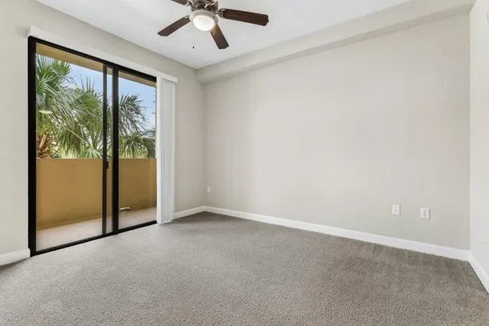 Large carpeted bedroom with ample room for furniture, ceiling fan, and ample natural light provided by sliding door leading out to private patio at Lantower Westshore.