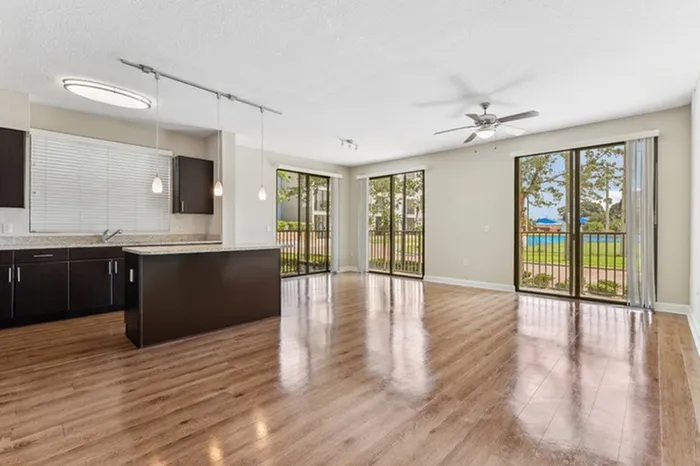 Kitchen with granite countertops, espresso-colored cabinets, stainless steel appliances, tile backsplash, wood-style flooring, pendant lighting, large island, and view living area with natural light from three large floor-to-ceiling windows at Lantower Westshore.