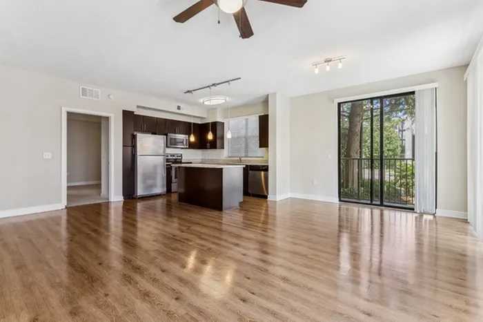 Spacious open-concept living area with natural light from three large floor-to-ceiling windows, wood-style flooring, ceiling fan, and view of kitchen at Lantower Westshore.
