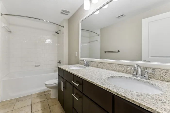 Large and bright bathroom with granite countertop, espresso-colored cabinetry, double sinks, large mirror, tile flooring, and tiled shower tub combo at Lantower Westshore.