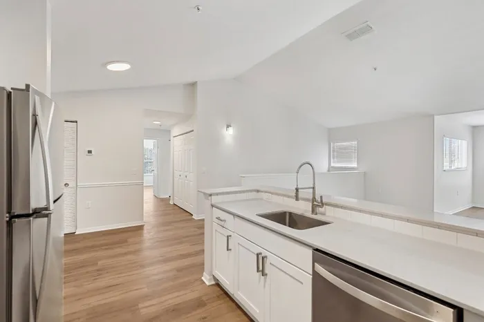 Apartment at Lantower Tortuga Bay with open-concept kitchen featuring white quartz counters, stainless steel appliances, white shaker-style cabinets, deep under-mount sink, wood plank floors, and recessed lighting.