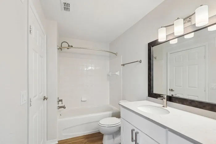 Large bathroom with white quartz countertops, white tiled shower tub combo, wood plant floors, bright lighting, and a framed mirror at Lantower Tortuga Bay.