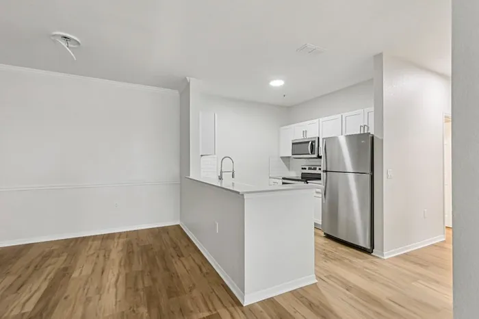 Open-concept kitchen at Lantower Tortuga Bay with white quartz counters, stainless steel appliances, white shaker-style cabinets, deep under-mount sink, wood plank floors, and recessed lighting.