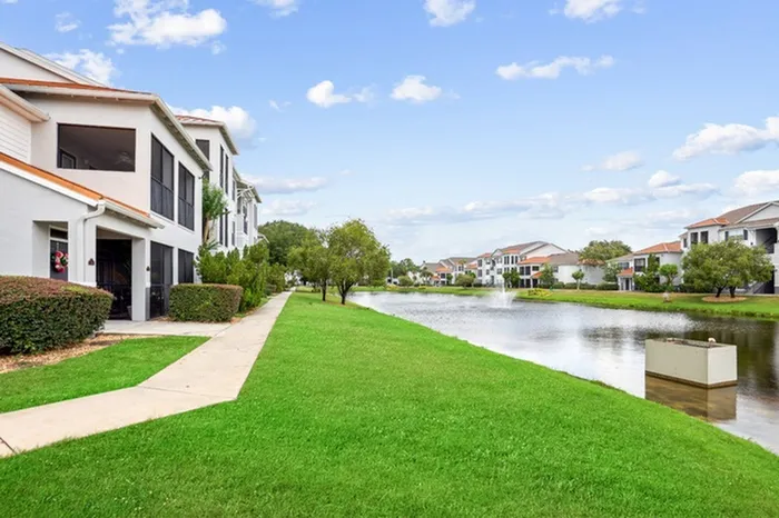Lush landscaping with palm trees, green grass, and water front feature at Tortuga Bay Apartments in Orlando, FL.