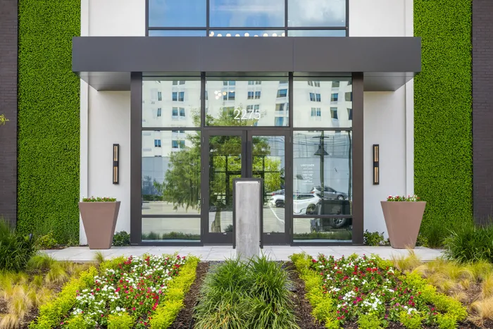 Modern apartment entrance with sleek glass doors, vibrant green walls, and a beautifully arranged floral garden.