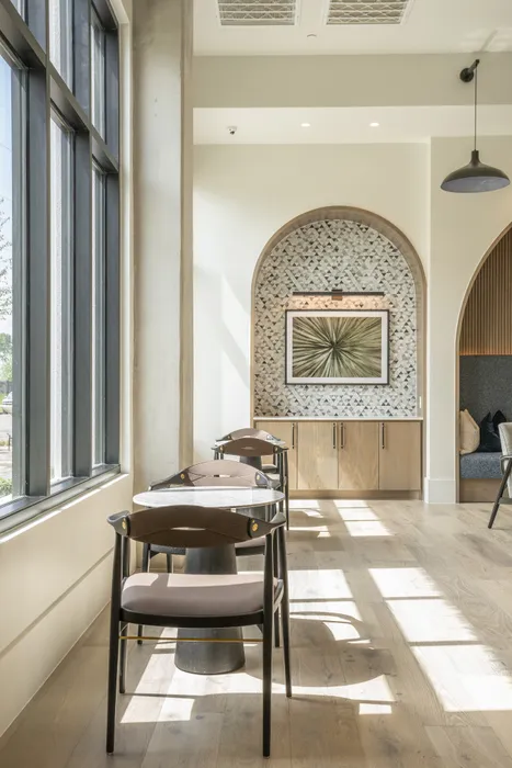 Bright, modern seating area with elegant chairs and tables in a chic apartment, featuring large sunlit windows and stylish decor.