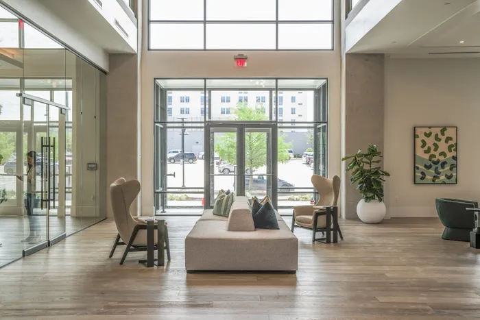 Modern apartment lobby with high ceilings, large windows, elegant seating, and contemporary decor.
