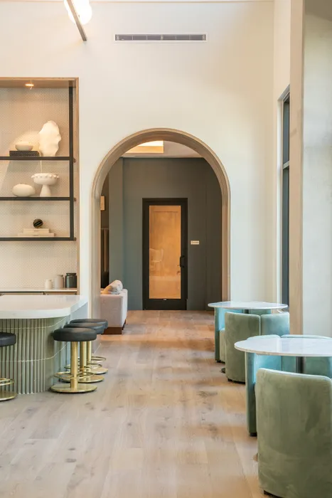 Elegant apartment interior featuring a stylish bar area with modern stools, decorative shelving, and a welcoming archway leading to a cozy room with plush seating.