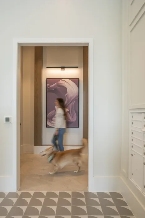 Elegant hallway with modern abstract artwork, featuring stylish tiled flooring and a woman walking her dog, adding a welcoming touch.