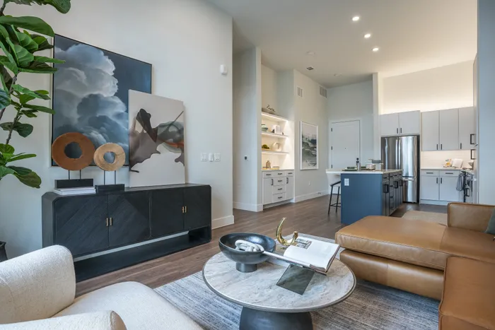 Modern living space with elegant decor, featuring an open-concept layout, luxurious brown leather sectional, and stylish kitchen with sleek appliances.
