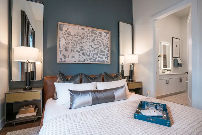 Modern bedroom with elegant decor, featuring a cozy bed with luxurious pillows, ambient lighting, and a chic bathroom entry.