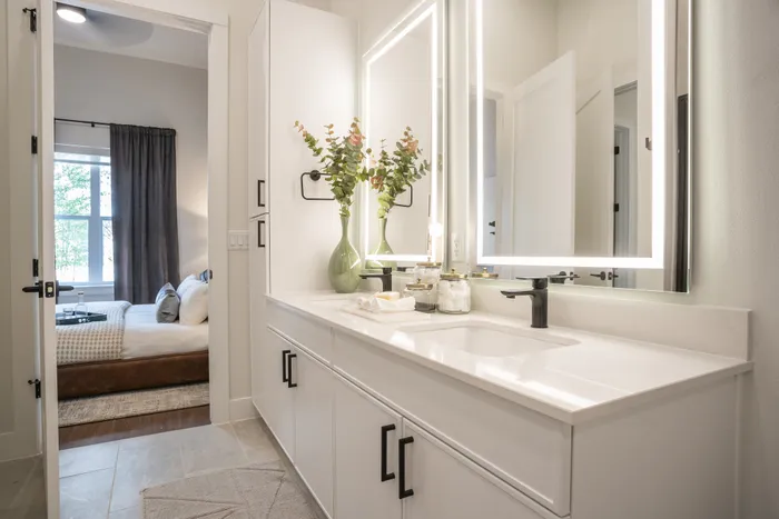 Elegant bathroom with sleek white cabinets and a designer vanity, opening into a cozy bedroom with natural light and modern decor.