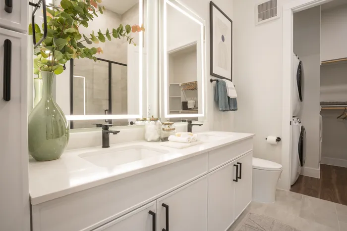 Luxurious bathroom featuring modern double vanity with elegant lighting, lush greenery, and convenient in-unit laundry.