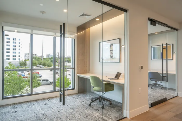 Bright and inviting modern office space with glass walls, featuring sleek furniture and ample natural light from large windows.