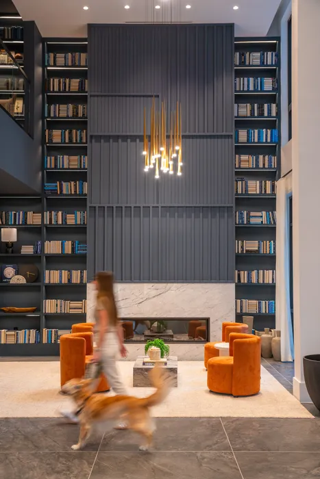 Elegant modern library with tall bookshelves, warm lighting, and plush orange seating, creating a welcoming and sophisticated ambiance.