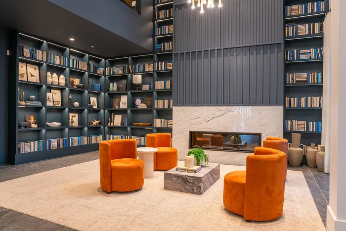 Modern living space with vibrant orange chairs, elegant shelves filled with books and decor, and a sleek marble fireplace for a cozy ambiance.