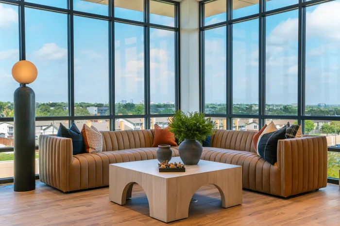 Elegant sunlit living area with panoramic windows, featuring a stylish leather sectional and a modern coffee table adorned with decorative plants.