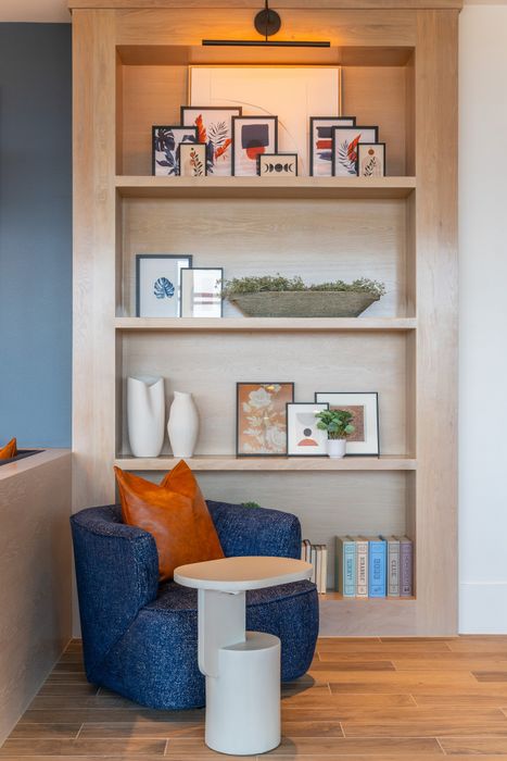 Inviting reading nook with a cozy blue chair, modern side table, and stylish shelving adorned with art and decor.