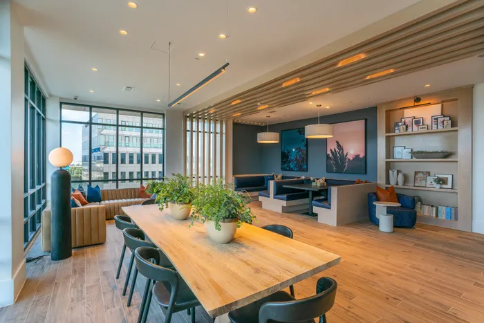 Contemporary open-concept living space featuring elegant dining area, cozy seating with vibrant cushions, and urban city views through large windows.