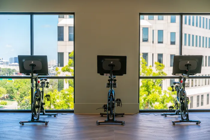 Modern gym room with three high-tech exercise bikes facing large windows, showcasing a vibrant city view.