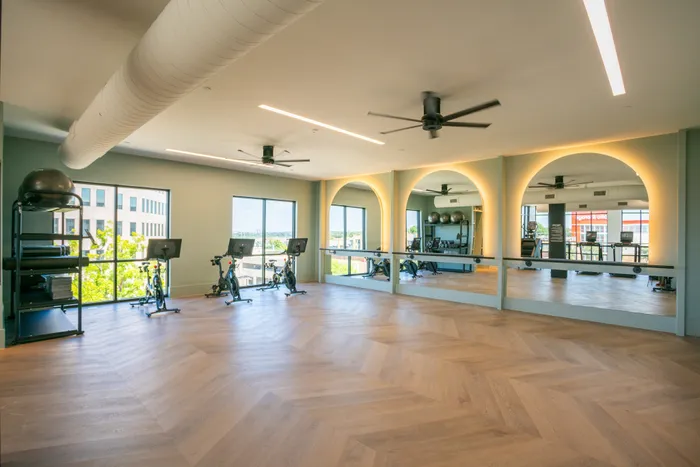 Sleek home gym with mirrored walls and modern exercise bikes, featuring stylish herringbone flooring and large windows for natural light.