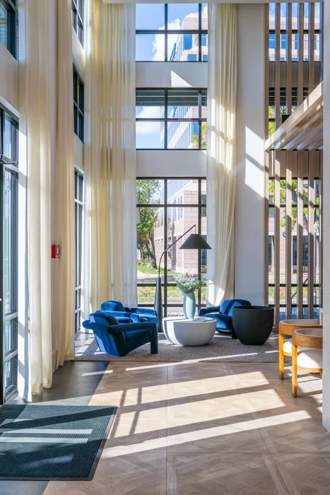 Bright and modern lobby with tall windows, elegant blue velvet chairs, and stylish decor, offering a welcoming and luxurious atmosphere.