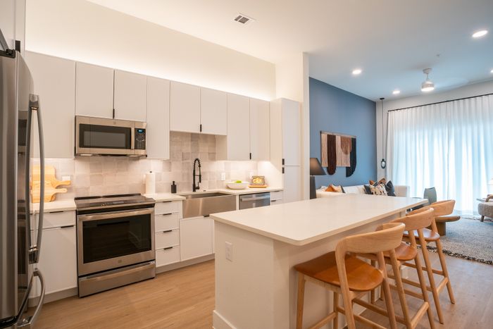 Modern open-concept kitchen with sleek cabinetry, stainless steel appliances, and a stylish breakfast bar extending into a cozy, well-lit living area.