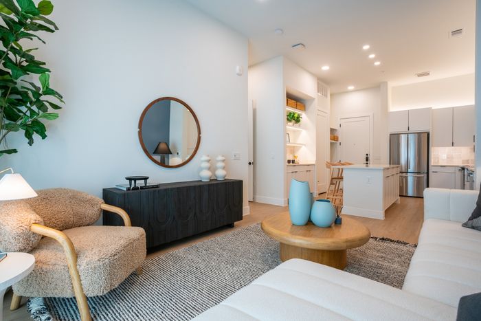 Contemporary living room featuring cozy shearling chair, elegant round mirror, and modern decor. Open-concept kitchen with sleek appliances and breakfast bar, ideal for entertaining.