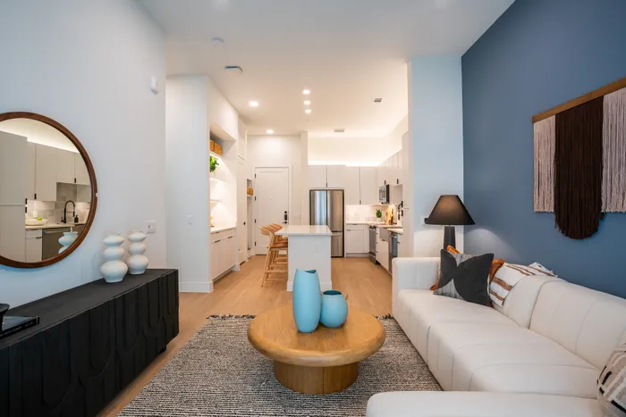 Modern open-concept living space featuring a chic white sofa, elegant round mirror, and stylish kitchen with a central island.