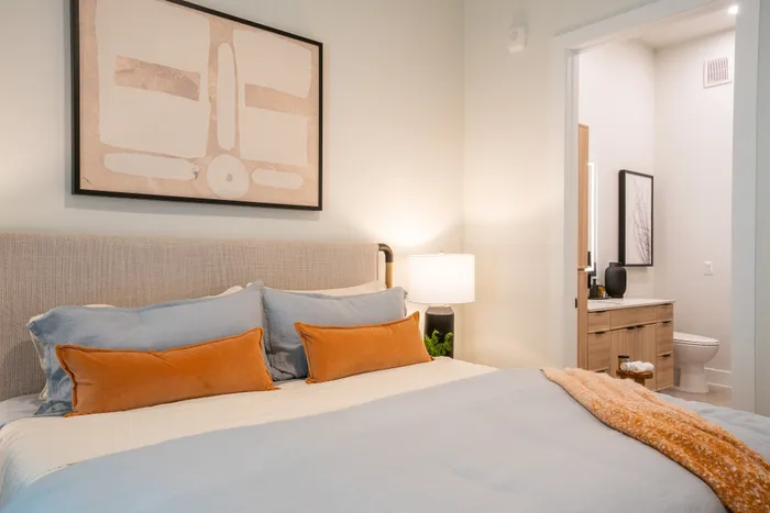 Cozy bedroom with elegant decor, featuring a comfortable bed with plush pillows and a warm lamp next to a modern en-suite bathroom.