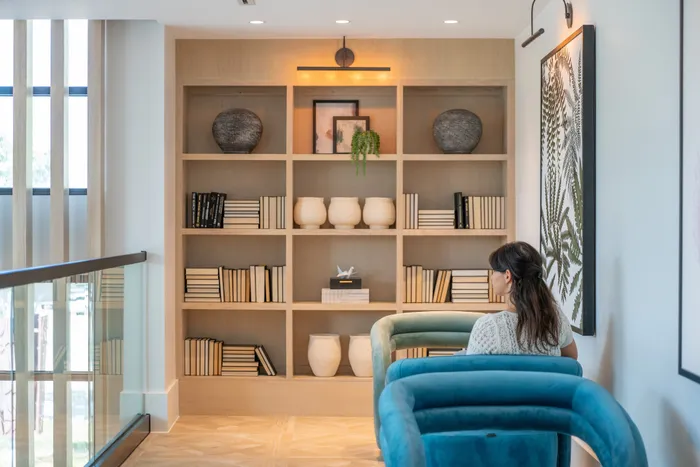 Contemporary living area with elegant bookshelf, cozy teal armchairs, and artistic décor for stylish apartment living.
