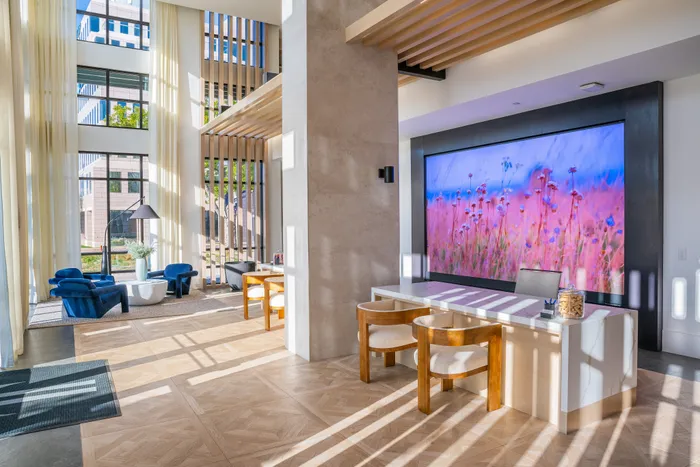 Bright and contemporary apartment lobby featuring elegant wooden accents, plush blue chairs, and a stunning floral art display. Abundant natural light streams through large windows, highlighting the chic design.