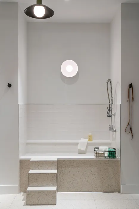 Modern bathroom featuring a sleek white bath with tiled steps, stylish wall lighting, and a contemporary shower fixture, creating a serene and inviting space.