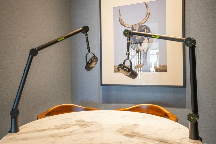 Modern podcast recording setup with two Shure microphones on adjustable arms over a sleek marble table, complemented by stylish artwork in the background.