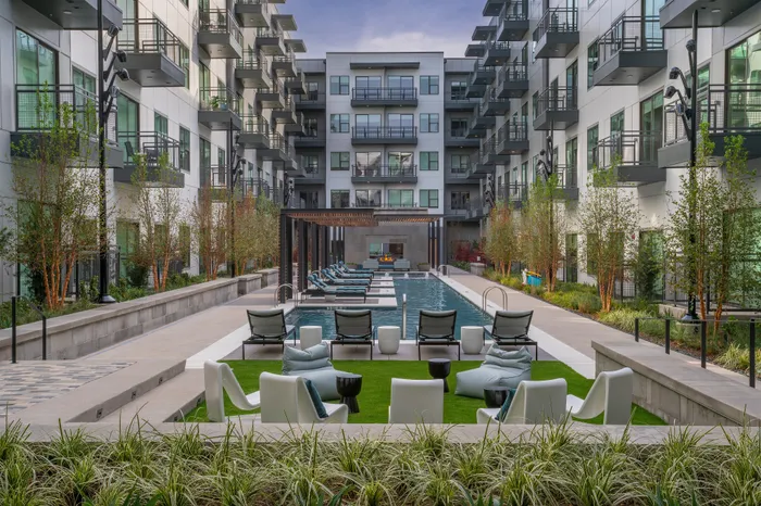 Modern apartment complex showcasing a luxurious pool area with stylish lounge chairs and vibrant landscaping, perfect for relaxation and social gatherings.