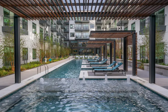 Luxurious apartment complex featuring a serene outdoor pool with modern lounge chairs and stylish pergolas.